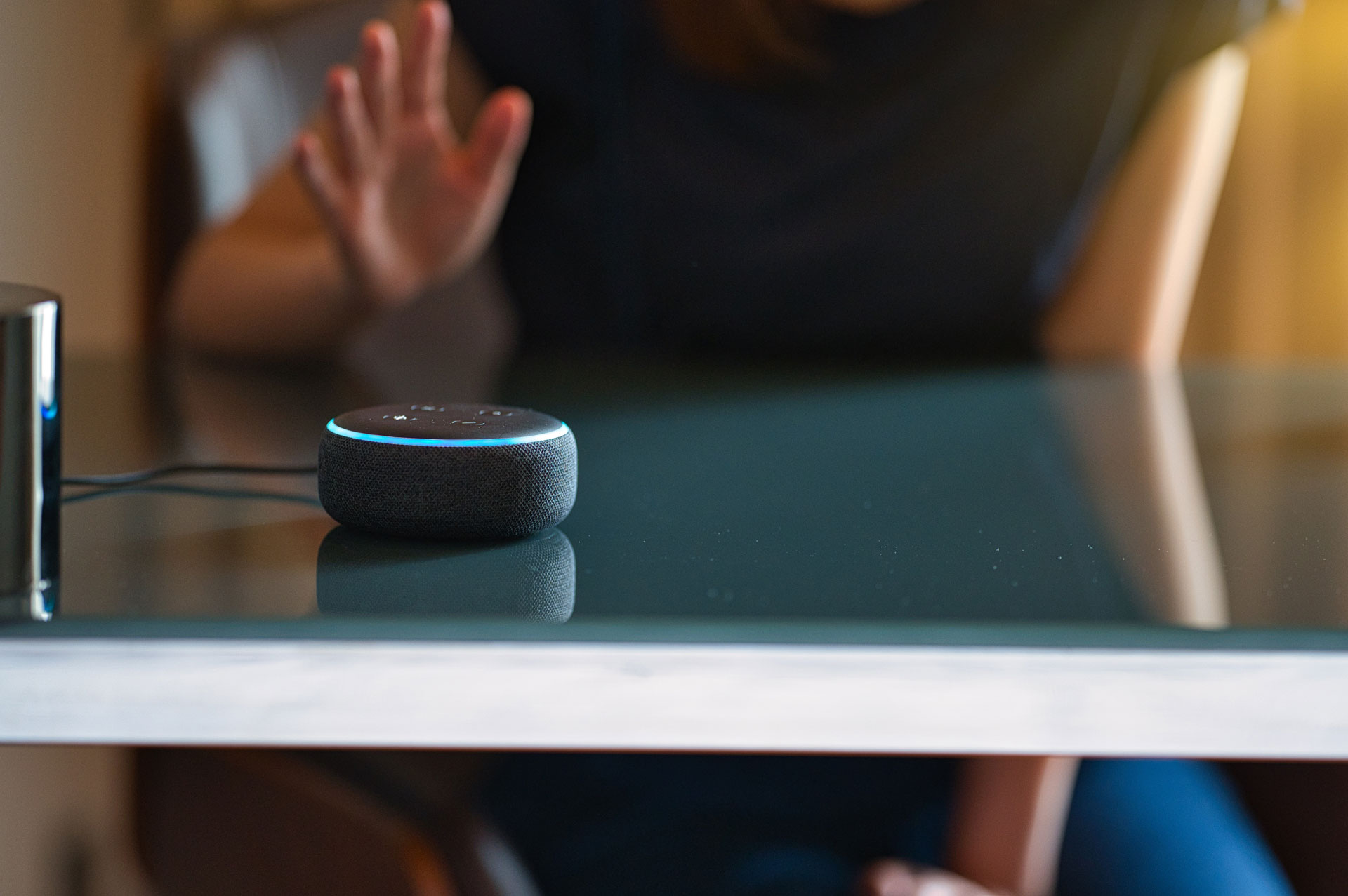 person at a desk speaks to a voice assistance device